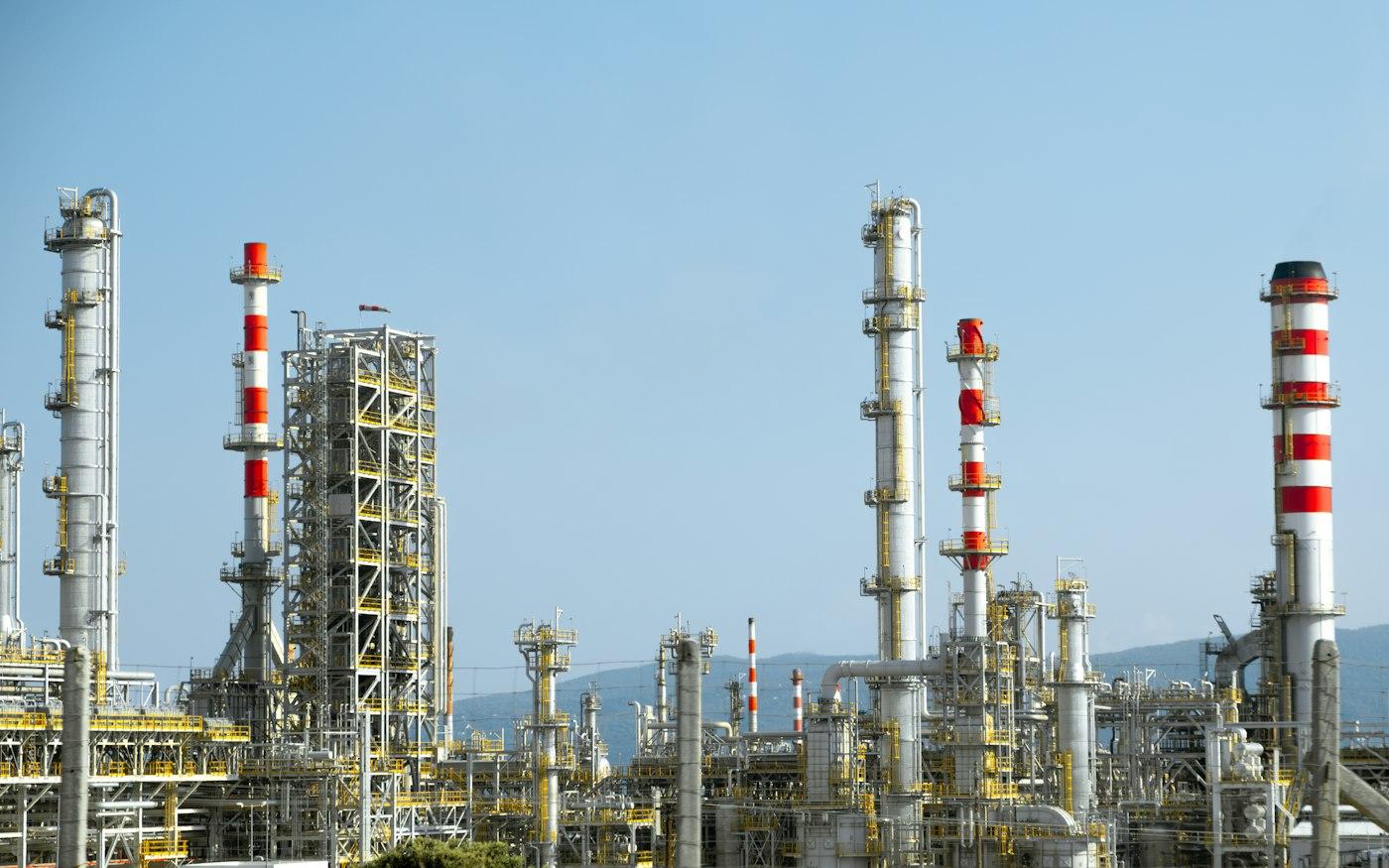 Oil refinery towers with red and white stacks under a clear sky